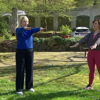 Moderatorin Heike Greis macht unter Anleitung einer Frau Übungen und streckt die Arme nach vorne aus.