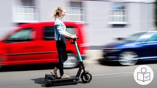 Eine Frau fährt auf einem E-Scooter auf der Straße. Im Hintergrund stehen Autos. In der Pfalz passieren immer mehr Unfälle mit E-Scootern. Rechts das SWR Logo für Leichte Sprache.