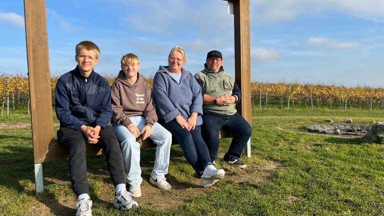 Eine Frau, ein Mann und zwei Jungs sitzen auf einem Holzrahmen auf einer Wiese.