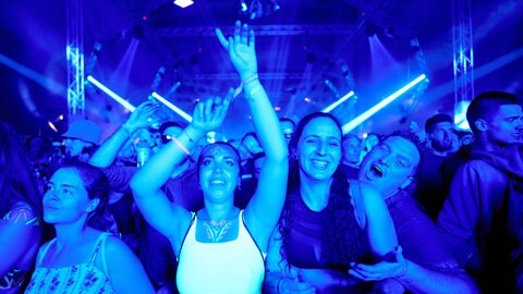 Besucherinnen und Besucher tanzen vor einer Festivalbühne.