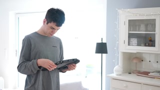 Elias steht im Raum und schaut auf sein Handy. Er ist eins von vielen Kindern mit Autismus, die Unterstützung brauchen.
