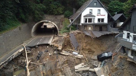 Eine zerstörte Straße mit kaputten Häusern und einem Tunnel. Die Bundesstraße, die durch das Ahrtal führt, ist hinter dem Tunnel in Altenahr durch die Flut weggerissen worden
