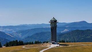 Der Feldbergturm im Sonnenschein. Im Hintergrund sind Berge.