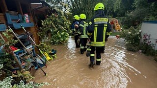 Feuerwehrleute laufen nach dem Unwetter durch einen völlig überschwemmten Garten zu einem Haus in Wachenheim.