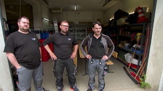 Drei Techniker stehen vor einer kleiner Lagerhalle