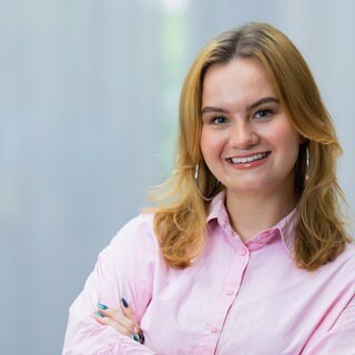 SWR-Reporterin Cosima Galm trägt ein rosa Hemd und steht vor einem weißen Hintergrund.