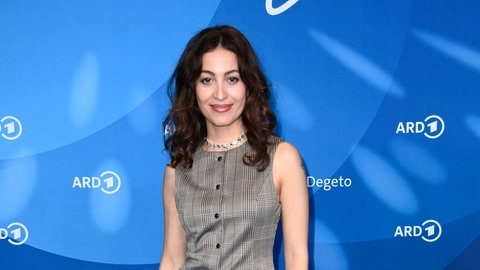 Sabrina Amali steht im Kostüm vor einer ARD Pressewand und lächelt