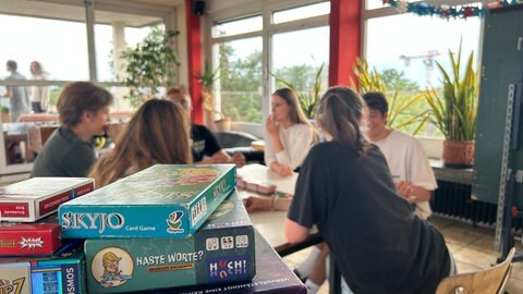 Sechs Studentinnen und Studenten bei ihrem wöchentlichen Spieleabend in Karlsruhe. Sie spielen ein Brettspiel auf einem Tisch.