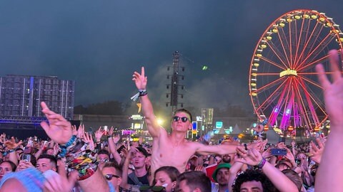Menschenmenge vor der Bühne, die zur Musik tanzt. Im Hintegrund ein beleuchtetes Riesenrad.