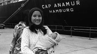 Eine junge Frau mit Kind steht vor demm Rettungsschiff "Cap Anamur"