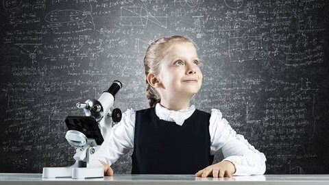Kleines Mädchen Wissenschaftlerin mit Mikroskop auf Kreidetafel Hintergrund. Bedarf an Lehrkräften wird es den kommenden Jahren vor allem auch in en sogenannten MINT-Fächern geben, also Fächern wie Mathematik oder Physik.