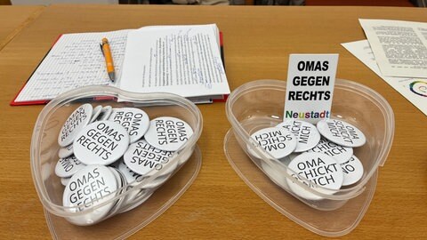 Buttons mit der Aufschrift "Omas gegen Rechts" und "Oma schickt mich" liegen in herzförmigen Plastikdosen