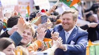 König William Alexander begrüßt beim Königstag in den Niederlanden die Menschen, die ihm zujubeln. Viele sind orange gekleidet. 