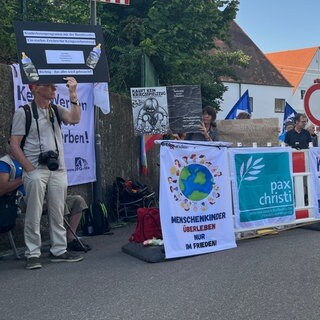 Menschen halten im bayerischen Kellmünz Banner und selbstgebastelte Plakate in die Höhe. Ein Ferienprogramm der Bundeswehr sorgt dort bei Friedensaktivisten und -aktivistinnen für Kritik.
