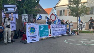 Menschen halten im bayerischen Kellmünz Banner und selbstgebastelte Plakate in die Höhe. Ein Ferienprogramm der Bundeswehr sorgt dort bei Friedensaktivisten und -aktivistinnen für Kritik.