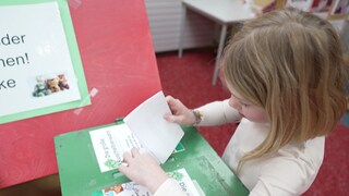 Ein kleines Mädchen wirft ihren ausgefüllten Wahlzettel zur Kuscheltierwahl in die grüne Wahlurne.