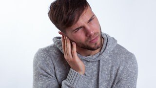 Junger Mann hält sich das Ohr: Was passiert bei einem Tinnitus und wie entsteht er?