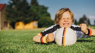 Kleiner junge mit Fußball drückt kräftig beide Daumen: Woher kommt die Redewendung "jemandem die Daumen drücken"?