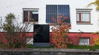 Wärmepumpe vor Privathaus zwischen herbstlichen Sträuchern