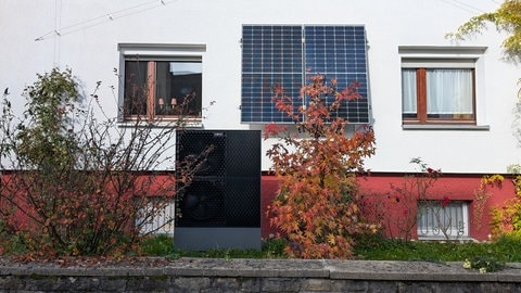 Wärmepumpe vor Privathaus zwischen herbstlichen Sträuchern