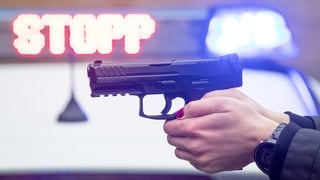 Eine Polizistin hält eine Dienstwaffe in der Hand (Symbolbild). In Pfedelbach schleift eine Frau mit ihrem Auto einen Polizisten mit. Beamte stoppen sie mit Schüssen. 