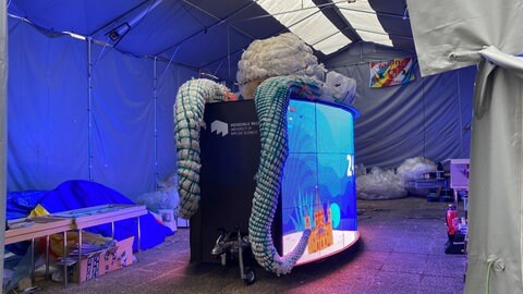 In einem Zelt steht eine LED-Wand, obendrauf ein halbfertiger Oktopus aus Plastik.