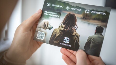 Eine Person hält einen Flyer des Sanitätsdienstes der Bundeswehr zum Thema posttraumatische Belastungsstörungen.