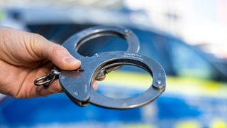 Handschellen vor einem Polizeiwagen.