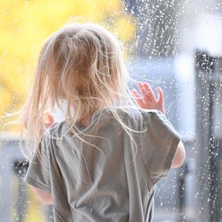 Ein Kind steht an einem Fenster mit Regentropfen