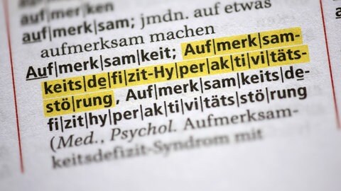 Nahaufnahme eines deutschen Wörterbuchs mit gelbmarkierten medizinischen Fachbegriff für ADHS "Aufmerksamkeitsdefizit-Hyperaktivitätsstörung". Auf Social Media und in der Wissenschaft wird häufig über die Erkrankung debattiert.