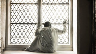 Frau in weißem Nachthemd am vergitterten Fenster einer Psychiatrie (Symbolbild): Bis in die 1970er-Jahre glichen Psychiatrien elenden Verwahranstalten: Patienten wurden ruhiggestellt, weggesperrt und unter menschenunwürdigen Bedingungen untergebracht.