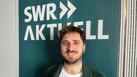 Moritz Braun steht vor dem Logo von SWR Aktuell