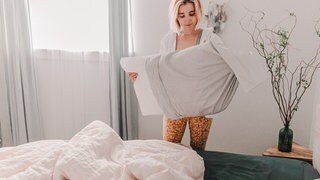 Frau bezieht Bett frisch