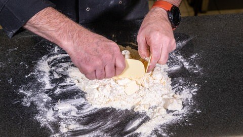 Ein feiner Boden für den Rhabarberkuchen: Den Mürbteig vermengt man auf der Arbeitsfläche mit Teigschabern.