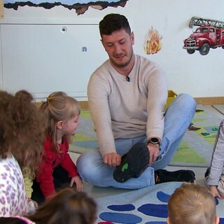 Erzieher Andrés sitzt in der Kita inmitten von Kindern.