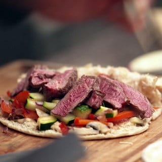 Mehrere rosa Steak-Stücke liegen auf Grillgemüse in einem Fladenbrot.