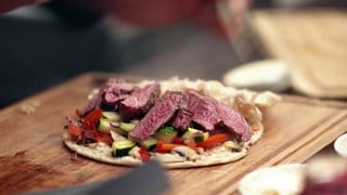 Mehrere rosa Steak-Stücke liegen auf Grillgemüse in einem Fladenbrot.