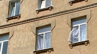 Fassade eines alten Mietshauses. Ein Fenster ist geöffnet, bei dem die Gardine herausweht.