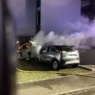 Zwei Feuerwehrleute löschen ein brennendes Auto