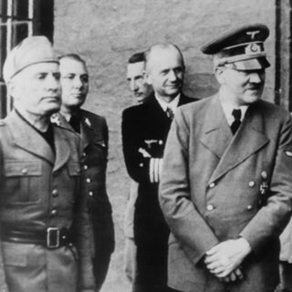 Adolf Hitler, der nach dem gescheiterten Attentat vom 20. Juli 1944 einen Verband an der linken Hand trägt. Von links:  Mussolini, Martin Borman, unbekannt, Adm. Dönitz, Hitler, Göring, Hermann Fegelein und Bruno Loerzer