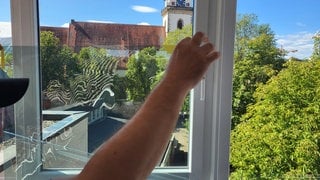An einem Wellenmuster vor einer sauberen Scheibe erkennt man, dass eine Folie auf ein Fenster aufgetragen wird - sie soll Hitze abhalten. Im Hintergrund die Metzinger Martinskirche