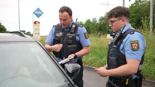 Zwei Polizeibeamte befragen eine Autofahrer auf einer Raststätte