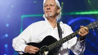 Johnny Logan: Der Sänger und mehrfache Sieger des ESC trägt ein weißes Hemd, passend zu seinem weißen Haar. Er spielt auf einer Gitarre