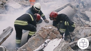 Drei Hilfs·kräfte stehen zwischen Trümmern. Die Hilfs·kräfte haben Arbeits·kleidung an. Trümmer sind zum Beispiel kaputte Teile von Häusern nach einem Erd·beben. Rechts das SWR Logo für Leichte Sprache.
