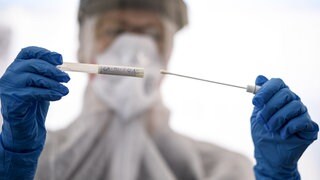 Frau im Schutzanzug hält ein Abstrichstäbichen für einen Corona-Test in der Hand