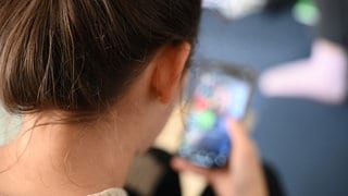 Blick über die Schulter: Eine 18-jährige Frau schaut gebannt auf ihr Handy