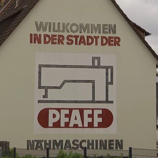 Auf einem Haus ist ein Werbeblock mit der Aufschrift: Willkommen in der Stadt der Pfaff Nähmaschinen