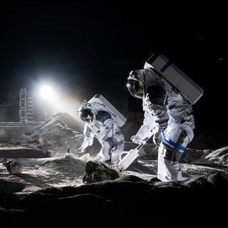 Übung in einer realistischen Mondumgebung in der LUNA-Einrichtung in Köln: Ein Experte für Bildanalyse dokumentiert einen simulierten Mondspaziergang, bei dem zwei Freiwillige mondähnliche Proben sammeln und analysieren.