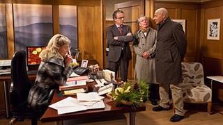Frau Heilert sitzt frierend an ihrem Schreibtisch, vor ihr stehen Franz, Herr Weiss und Bernhard