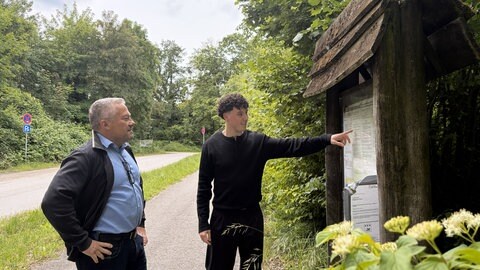 Der Dettenheimer Bürgermeister Frank Bolz und der stellvertretende Hauptamtsleiter Janik Schurr zeigen auf ein Schild Baggersee Giesen.